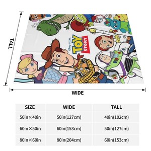 Może przedstawiać: Biały koc z kolorową grafiką Toy Story przedstawiającą postacie takie jak Woody, Buzz Astral, Jessie i Pastereczka. Pod kocem znajduje się tabela rozmiar&oacute;w z wymiarami w calach i centymetrach dla opcji 50x40, 60x50 oraz 80x60 cali.