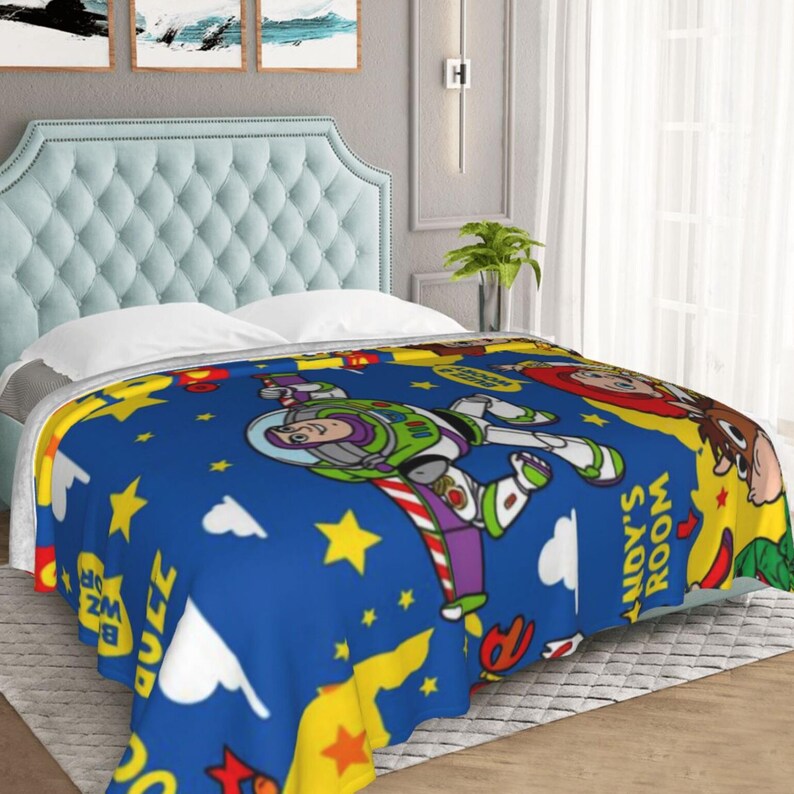 May include: A blue fleece blanket featuring a repeating pattern of Buzz Lightyear, Woody, and Jessie from Toy Story. The design includes yellow stars, white clouds, and the text "Andy's Room" printed in a bold yellow font against a vibrant blue background.