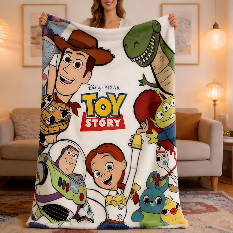 Może przedstawiać: Biały koc z polaru z logo Disney Pixar Toy Story pośrodku, otoczony kolorowymi ilustracjami Chudego, Buzza Astrala, Jessie, Rexa, Obcego, Sztućka, Kaczora i Kr&oacute;lika na miękkiej, teksturowanej powierzchni z tkaniny.
