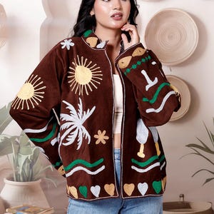 May include: A brown long-sleeve jacket featuring colorful embroidered motifs including yellow suns, white palm trees, green wavy lines, and alternating gold and silver heart shapes along the hem, worn over a white top and blue denim jeans.