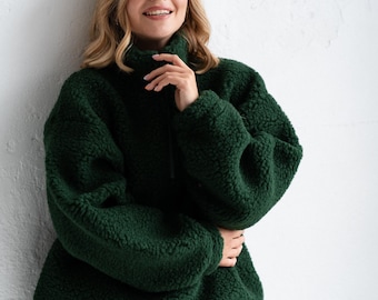 Può includere: Un maglione in pile verde bosco scuro con collo alto e chiusura a mezza zip. Il capo presenta un materiale spesso e testurizzato in stile sherpa, maniche lunghe con polsini a coste e una vestibilità ampia e rilassata.