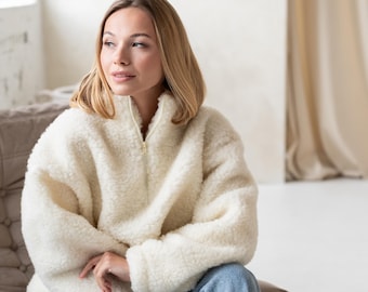 Può includere: Una giacca in pile color bianco sporco a maniche lunghe con collo alto e chiusura centrale con zip color oro. Il capo presenta un materiale testurizzato e soffice ed è abbinato a un paio di jeans in denim di colore azzurro.