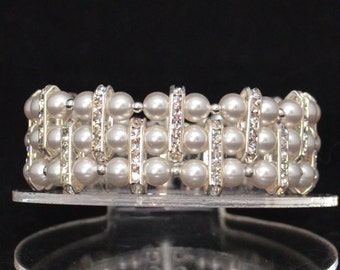 May include: A silver bracelet with white pearls and clear rhinestones. The bracelet is on a clear display stand.