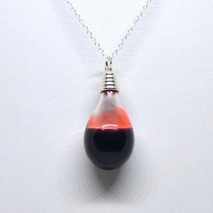 May include: A silver chain necklace with a glass pendant shaped like a teardrop. The pendant is filled with a dark red liquid and a small amount of red liquid is visible at the top of the pendant.