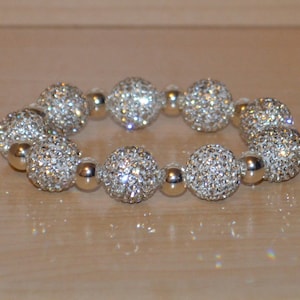 May include: A silver bracelet with round, sparkly beads. The beads are covered in small, clear rhinestones.