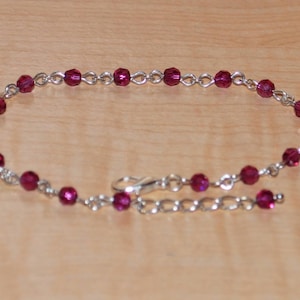 May include: A silver chain anklet with small, dark red crystal beads.