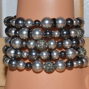 May include: A stack of six silver and black beaded bracelets. The bracelets are made with large, round beads and some have small, sparkly accents.