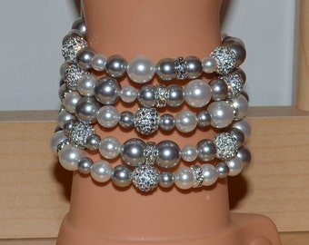 May include: A stack of six bracelets made with white and silver beads. Some of the beads are accented with rhinestones.