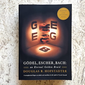 May include: A black book cover titled GÖDEL, ESCHER, BACH: an Eternal Golden Braid by Douglas R. Hofstadter. The cover features a glowing, three-dimensional letter G casting shadows, with a gold circular seal stating Winner of the Pulitzer Prize.