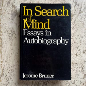 May include: A hardcover book titled "In Search of Mind" with the subtitle "Essays in Autobiography" by Jerome Bruner. The book has a black cover with yellow and white text.