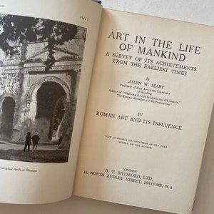 May include: Open book with the title "ART IN THE LIFE OF MANKIND" by Allen W. Seaby. The book's pages display text about Roman art and its influence, accompanied by a black and white photograph of a Roman arch. The book is published by B.T. Batsford, Ltd.