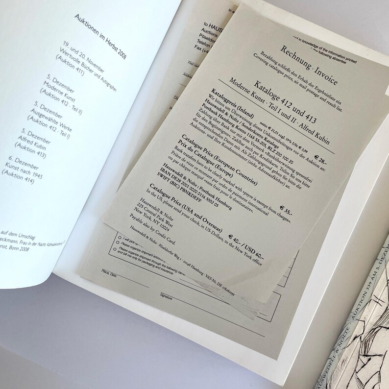 May include: A close-up of a document with the title "Rechnung Invoice" and the text "Moderne Kunst Teil I und II Alfred Kubin Kataloge 412 und 413" printed on it. The document lists prices for catalogs in different countries, including Germany, Europe, and the USA.