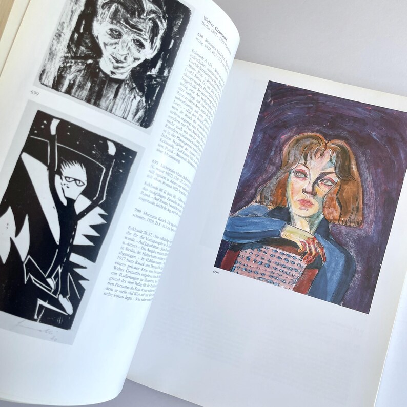 May include: A book open to a page with two black and white illustrations of people and a color illustration of a woman with brown hair. The text on the page reads "Walter Gramatt&eacute; 1897-1927."