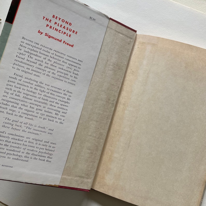 May include: A vintage book titled "Beyond the Pleasure Principle" by Sigmund Freud. The book cover is a light brown with black text. The book is open to the first page, showing the beginning of the text.