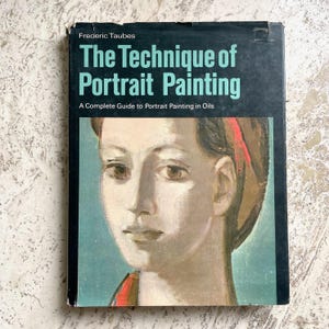 May include: A vintage book titled "The Technique of Portrait Painting" by Frederic Taubes. The cover features a portrait painting of a person with a red ribbon in their hair. The book is a complete guide to portrait painting in oils.