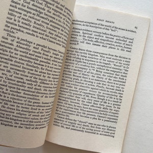 Może przedstawiać: Zbliżenie na książkę z białą okładką i czarnym tekstem. Tytuł książki to "First Essays", a tekst na okładce dotyczy filozofii Alberta Camusa.