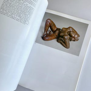 May include: A bronze sculpture of a reclining nude figure. The figure is lying on its side with its head resting on its arm. The sculpture is detailed and has a rough texture.