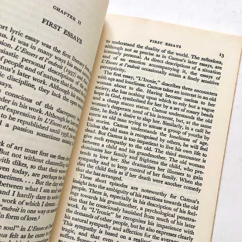 Może przedstawiać: Zbliżenie na książkę zatytułowaną "Pierwsze eseje" Alberta Camusa. Książka jest otwarta na stronie z tekstem "L'Ironie" i omawia dualizm świata oraz samotność starości.