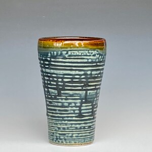 May include: A ceramic drinking glass with a blue and white striped pattern and a brown rim.