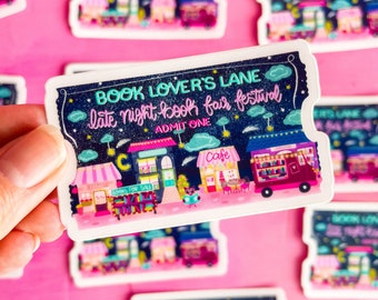 May include: A white ticket with a blue background and colorful illustrations of shops and a night sky. The text on the ticket reads "Book Lover's Lane Late Night Book Fair Festival Admit One".