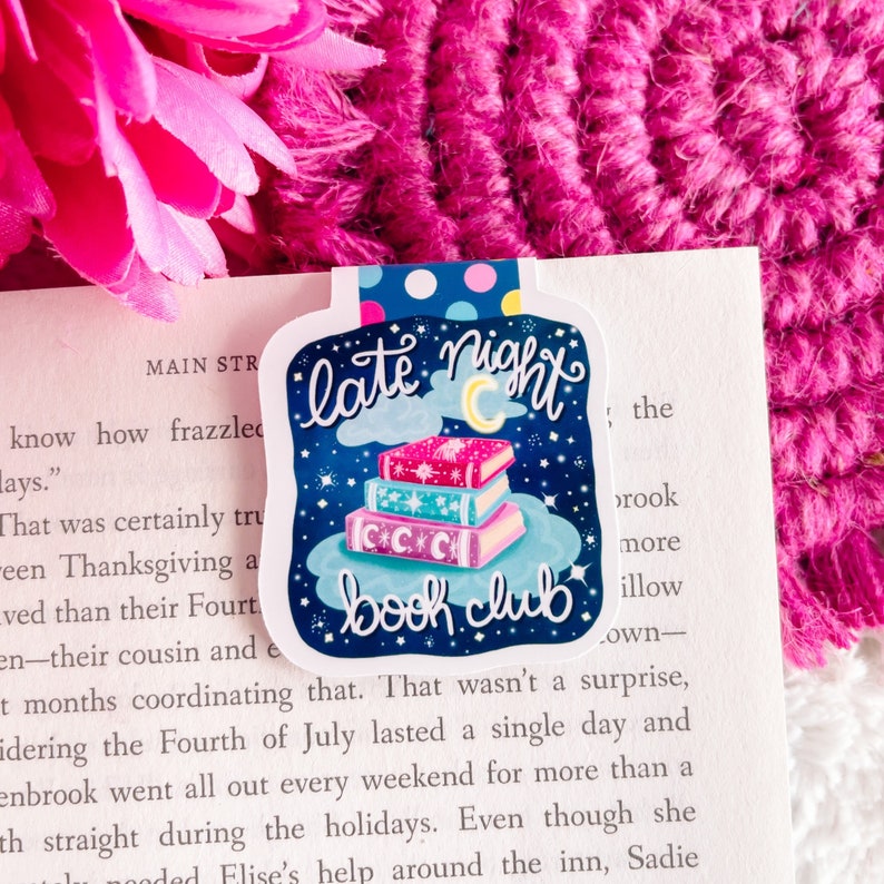 May include: A blue and white bookmark with a stack of books, a crescent moon, and stars. The text reads "late night book club".
