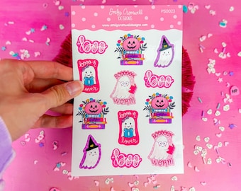 May include: A sheet of stickers featuring cute ghost illustrations with Halloween-themed sayings like "Boo-k lover" and "Boo-ook worm". The stickers are on a white background with pink accents.