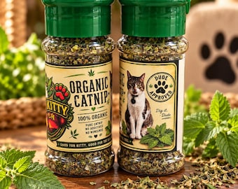 May include: Two clear plastic jars filled with dried green organic catnip, each topped with a dark green screw-on lid. The labels feature text including Organic Catnip, 100% Organic, and Dude Approved, along with an illustration of a cat.