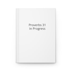 Puede incluir: Un diario blanco con el texto "Proverbs 31 In Progress" impreso en negro. El diario rectangular presenta un diseño limpio y minimalista, adecuado para escribir y tomar notas.