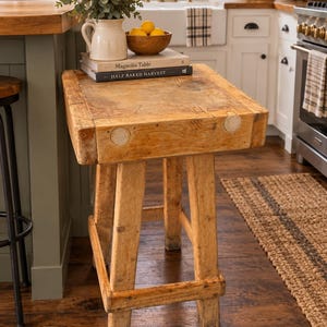 May include: A rustic, weathered wooden butcher block table with a thick, rectangular top and four sturdy legs connected by a lower support frame. The surface shows signs of heavy use, featuring a natural light brown wood grain and texture.
