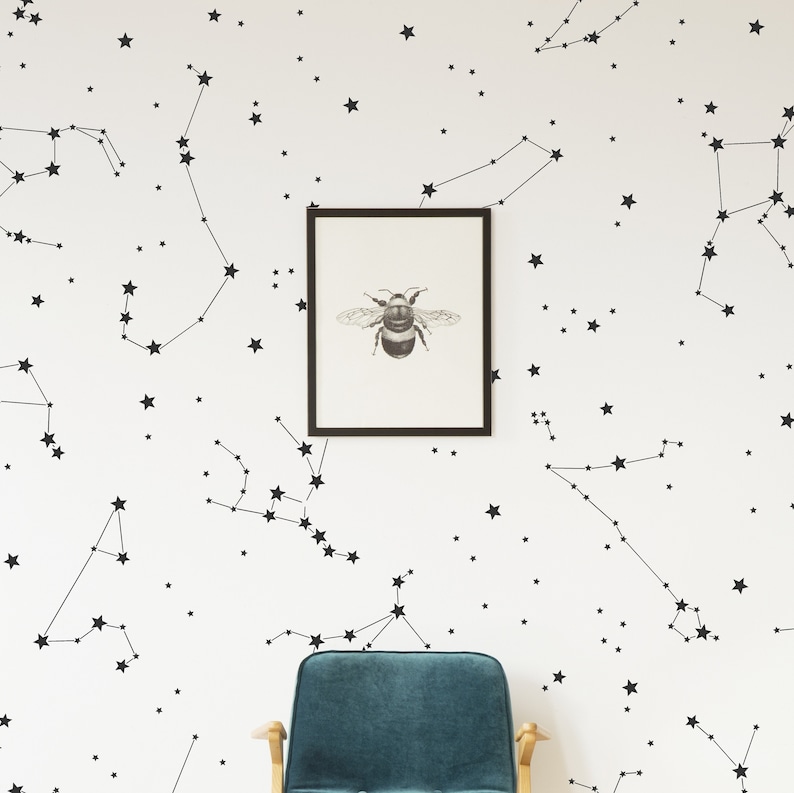 Puede incluir: Una pared blanca con constelaciones de estrellas negras y una impresi&oacute;n enmarcada de una abeja. Un sill&oacute;n azul teal est&aacute; en primer plano.