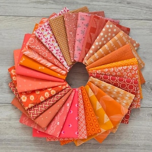 May include: A circular arrangement of folded fabric squares in various shades of orange, coral, and pink. The textiles feature diverse patterns including floral prints, geometric shapes, polka dots, stripes, and cross-hatching, displayed in a fan-like formation.