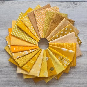 May include: A collection of folded fabric squares arranged in a circular fan pattern. The textiles feature various shades of yellow and gold, displaying diverse patterns including geometric shapes, floral motifs, stars, honeycomb, and linear designs.