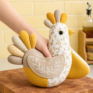 May include: A stuffed fabric chicken toy featuring a white body with a yellow floral pattern, yellow polka-dot wings, and a beige wing patch with white leaf embroidery. The crest consists of yellow and beige patterned fabric segments.