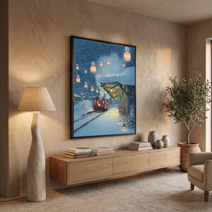 May include: A framed wall art print depicting a snowy winter scene with a red train arriving at a station platform illuminated by glowing lanterns. The artwork features deep blue night skies, white snow-covered ground, and festive greenery.