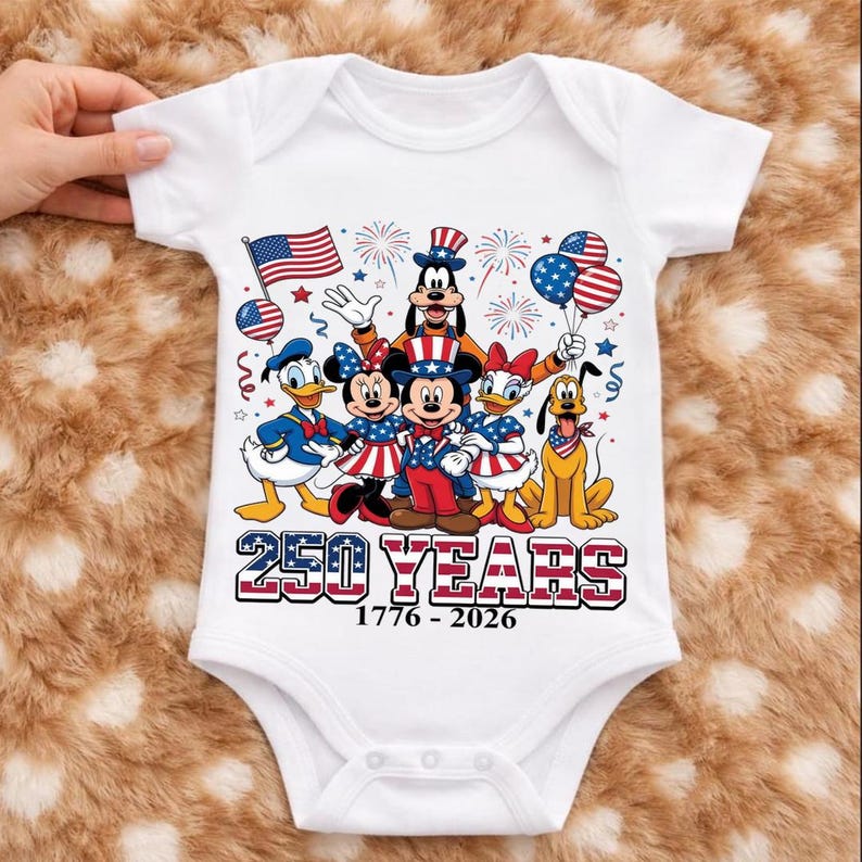 Może przedstawiać: Białe body niemowlęce z kr&oacute;tkim rękawem z grafiką postaci Disneya, w tym Myszki Miki, Minnie, Kaczora Donalda, Daisy, Goofy'ego i Pluto w patriotycznych strojach. Tekst głosi 250 YEARS 1776 - 2026 z motywami flagi amerykańskiej i fajerwerk&oacute;w.