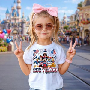 Może przedstawiać: Biały t-shirt z grafiką przedstawiającą postacie Disneya, w tym Myszkę Miki, Myszkę Minnie, Kaczora Donalda, Daisy, Goofy'ego i Pluto w patriotycznych strojach, z napisem 250 YEARS 1776-2026 oraz motywami amerykańskiej flagi.