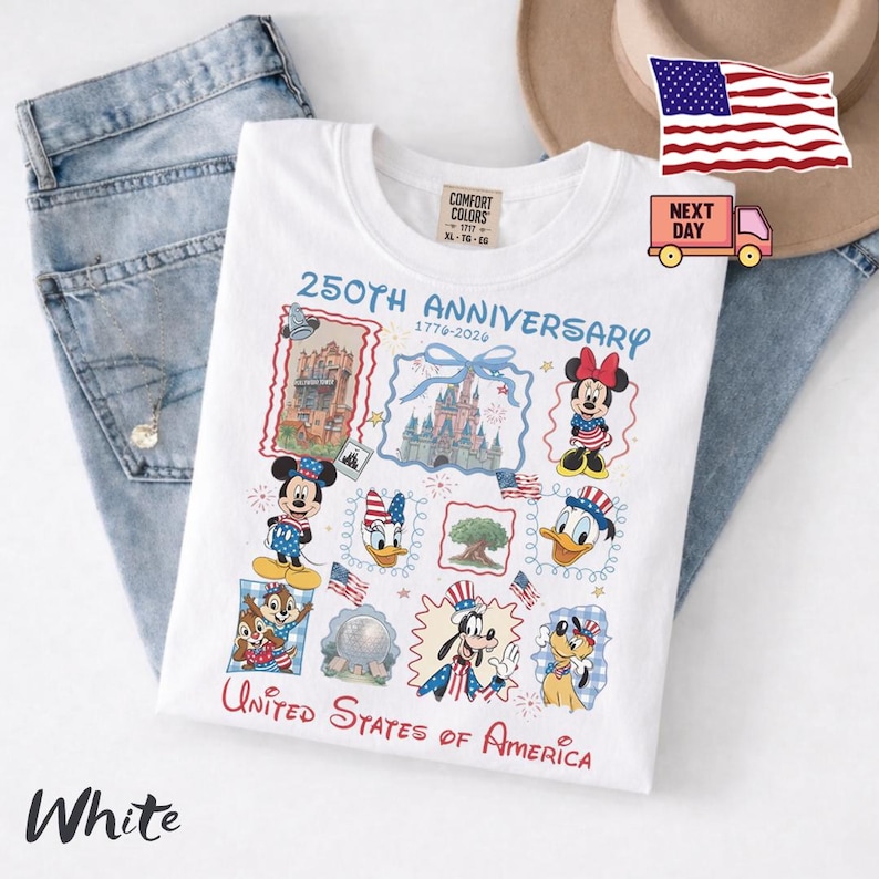Peut inclure: Un t-shirt blanc avec un motif 250th Anniversary 1776-2026 illustrant Mickey, Minnie, Donald, Daisy, Dingo, Pluto, Tic, Tac et divers monuments, accompagn&eacute; du texte United States of America imprim&eacute; sur le devant du v&ecirc;tement.