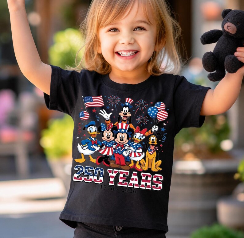 Może przedstawiać: Czarny t-shirt z kr&oacute;tkim rękawem z grafiką przedstawiającą postacie Disneya, w tym Myszkę Miki, Myszkę Minnie, Kaczora Donalda, Daisy, Goofy'ego i Pluto w patriotycznych strojach, z napisem 250 YEARS 1776-2026 oraz amerykańskimi flagami.