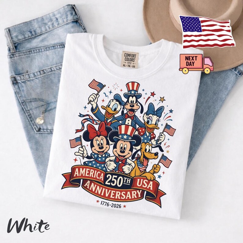 May include: A white t-shirt featuring a graphic of six cartoon characters wearing patriotic red, white, and blue outfits and holding American flags. Below the characters, a red banner displays the text America 250th Anniversary 1776-2026.