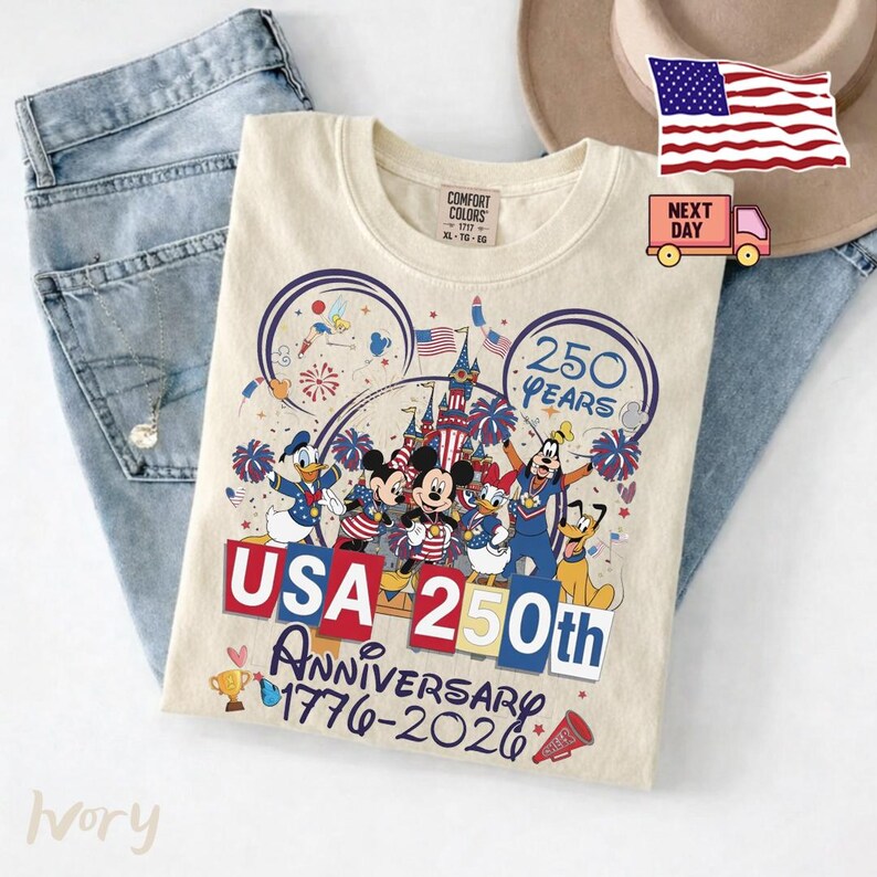 May include: An ivory t-shirt featuring a graphic of Disney characters including Mickey Mouse, Donald Duck, and Goofy in front of a castle. The text reads 250 YEARS, USA 250th ANNIVERSARY 1776-2026, with fireworks, American flags, and a trophy illustration.