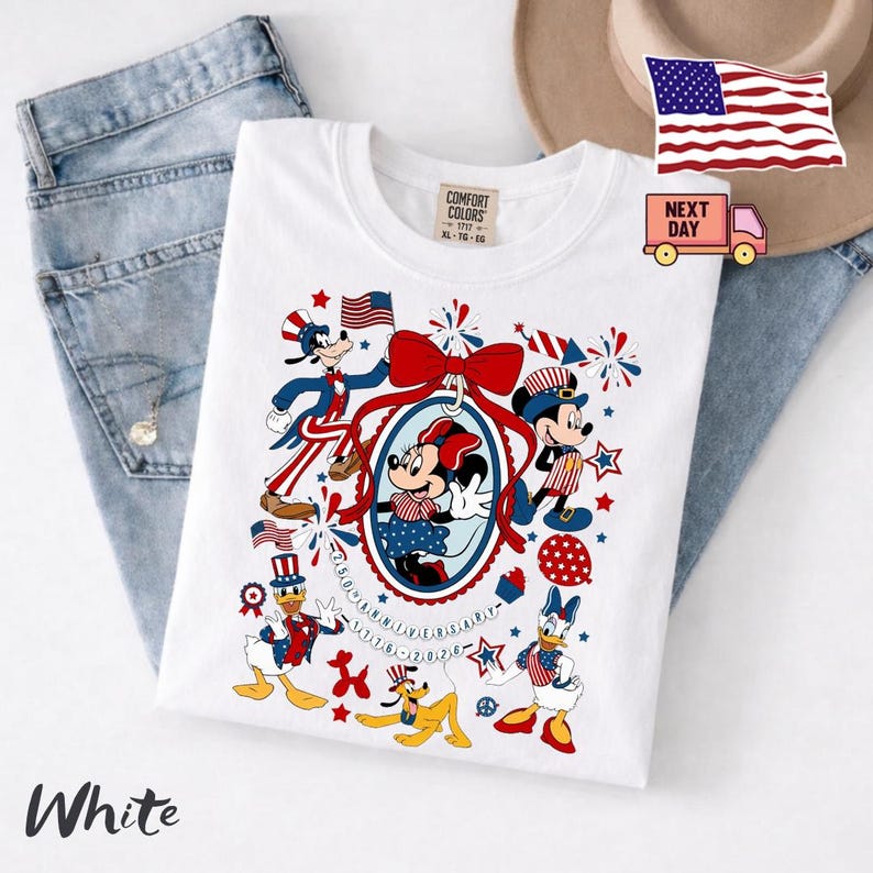 Może przedstawiać: Biały t-shirt z nadrukiem graficznym przedstawiającym postacie Disneya, w tym Myszkę Miki, Minnie, Kaczora Donalda, Daisy, Goofy'ego i Pluto w patriotycznych strojach w kolorach czerwonym, białym i niebieskim. Wz&oacute;r zawiera fajerwerki, gwiazdki i napis 250th Anniversary 1776-2026.
