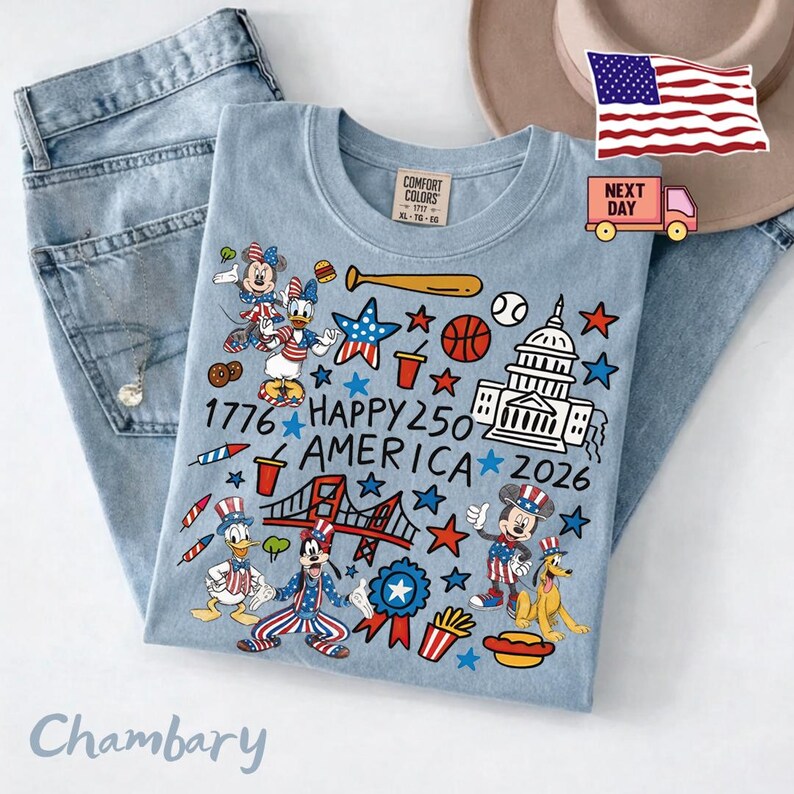 May include: A light blue t-shirt featuring a graphic print with Disney characters, the US Capitol building, a bridge, and patriotic symbols. The text reads 1776 HAPPY 250 AMERICA 2026. The shirt is displayed alongside light blue denim jeans.