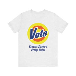 May include: White t-shirt with a graphic that says "Vote" in blue and yellow, resembling a detergent logo. Below the logo, the text reads "Removes Stubborn Orange Stains."