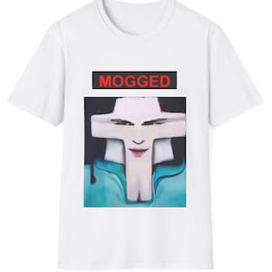 Puede incluir: Una camiseta blanca de manga corta con un estampado gráfico central. El diseño incluye un recuadro negro con el texto rojo MOGGED, situado sobre un rostro estilizado y distorsionado con forma de cruz y una sección inferior azulada.