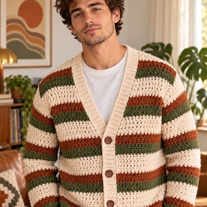May include: A long-sleeve crochet cardigan featuring horizontal stripes in cream, forest green, and burnt orange. The garment has a V-neckline, a ribbed cream-coloured button placket, and three large, round, dark brown buttons down the front.