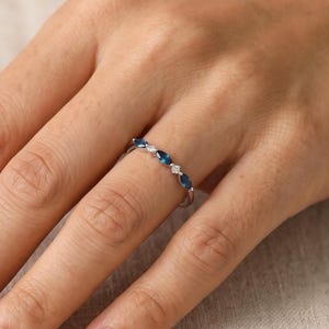 May include: A silver-toned ring featuring a delicate band set with alternating marquise-cut blue stones and small round clear stones. The stones are arranged in a linear pattern along the top half of the band, creating a refined and symmetrical look.