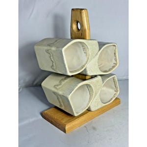 May include: A handmade, two-tiered ceramic wine rack with a wooden base and handle. The rack features four angled compartments for holding bottles. The ceramic is a light beige color with a textured surface, and the wood is a natural light brown.