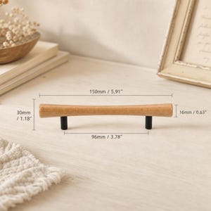 May include: A light brown wooden cabinet handle with two black cylindrical mounting posts. The handle measures 5.91 inches in total length, 1.18 inches in height, 0.63 inches in diameter, and has a 3.78-inch distance between the mounting posts.
