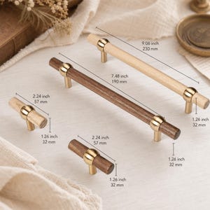 Pode incluir: Quatro puxadores cilíndricos para armários com acabamentos em madeira clara e escura e detalhes em metal dourado. Inclui dois puxadores pequenos de 57 mm de comprimento e dois longos de 190 mm e 230 mm, todos com 32 mm de altura.