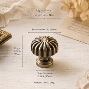 Könnte beinhalten: Ein kleiner, einlöchriger Messingknopf mit geriffeltem, kreisförmigem Design. Der Knopf hat einen Durchmesser von 25 mm, eine Höhe von 25 mm und einen Basisdurchmesser von 15 mm. Er wiegt 48 g und hat ein dunkles, antik wirkendes Finish.